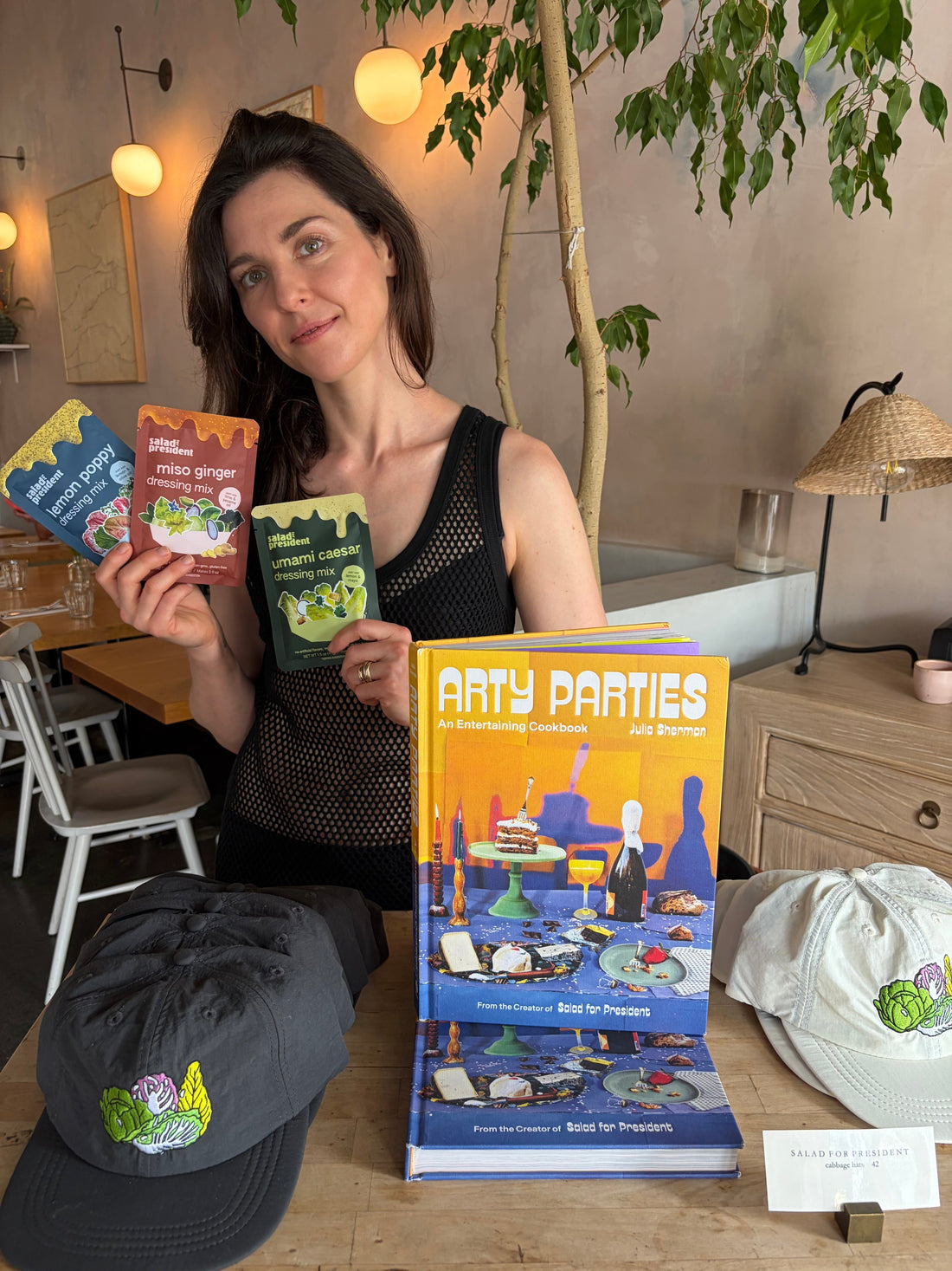 Julia Sherman, founder of Salad for President, posing with her new powdered salad dressings, her book Arty parties, and Cabbage Hats. 